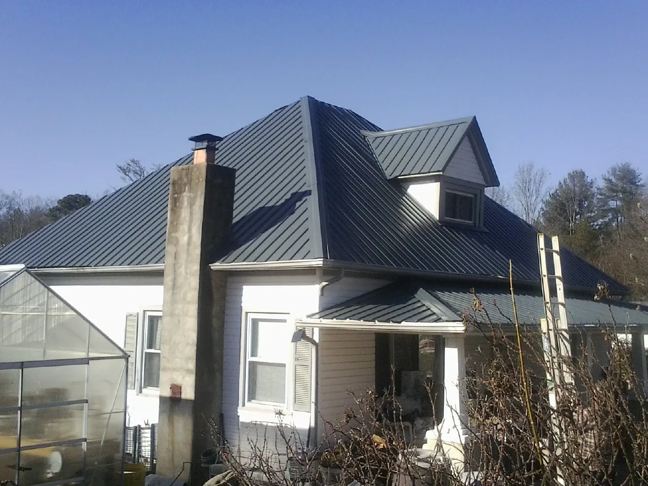 Dark blue standing seam metal roof on a white farmhouse with dormer — Slate & Tile Roof Repair by Roofing Brothers in Carey