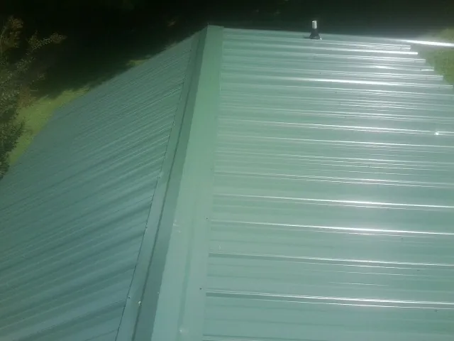 New green metal panels meeting at the ridge of a roof — Flat Roof Repair work by our crew in Carey