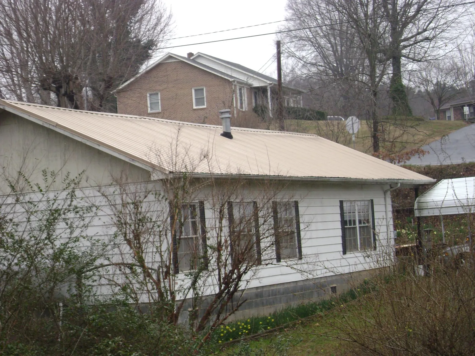 Tan metal roof on a white sided house set into a hillside — Commercial Roofing by Roofing Brothers in Carey